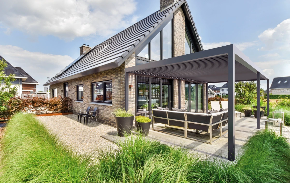 Pergola ogrodowa nad tarasem z przeszklonymi drzwiami przesuwnymi i meblami wypoczynkowymi