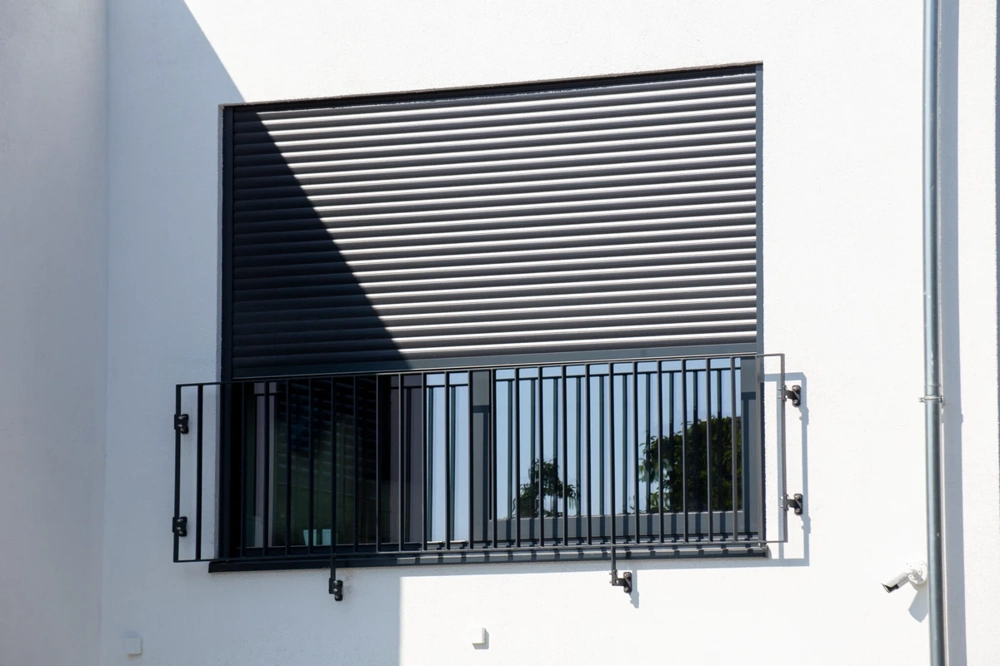 Białe elewacyjne okno z aluminiowymi roletami zewnętrznymi i metalową balustradą